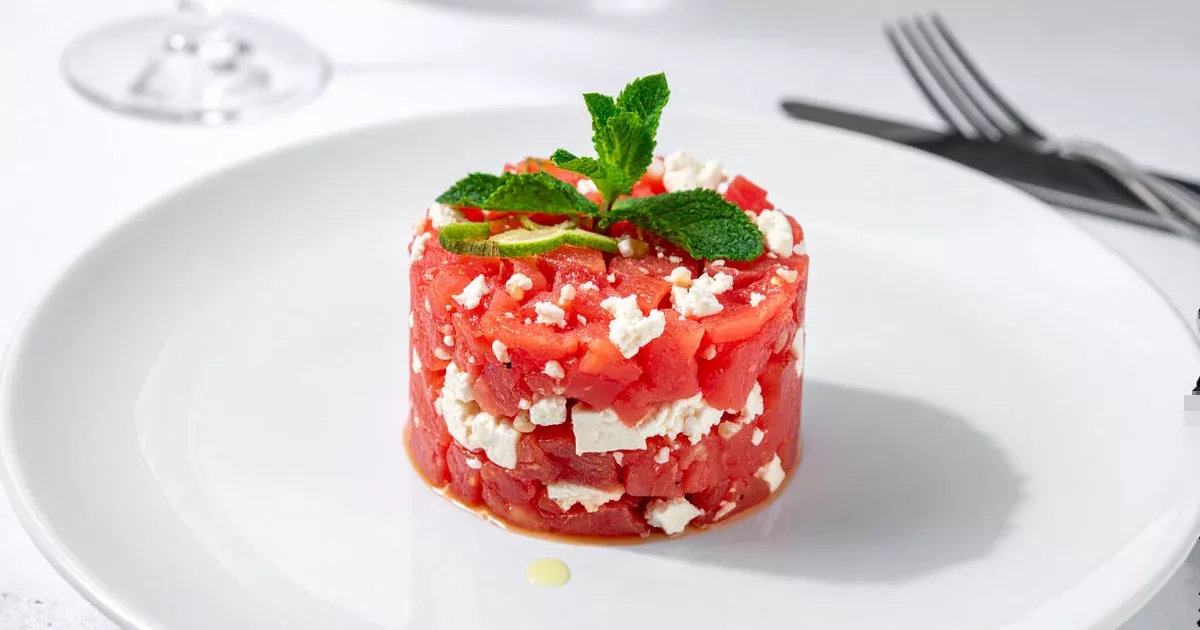 Feta-Wassermelone-Tatar mit Minze und Limette, angerichtet auf einem Teller mit Servierring