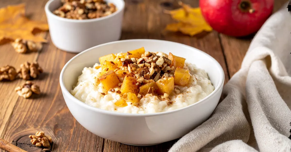 Herbstlicher Protein-Milchreis mit Apfelstücken, Zimt und Walnüssen in einer weißen Schüssel auf Holztisch