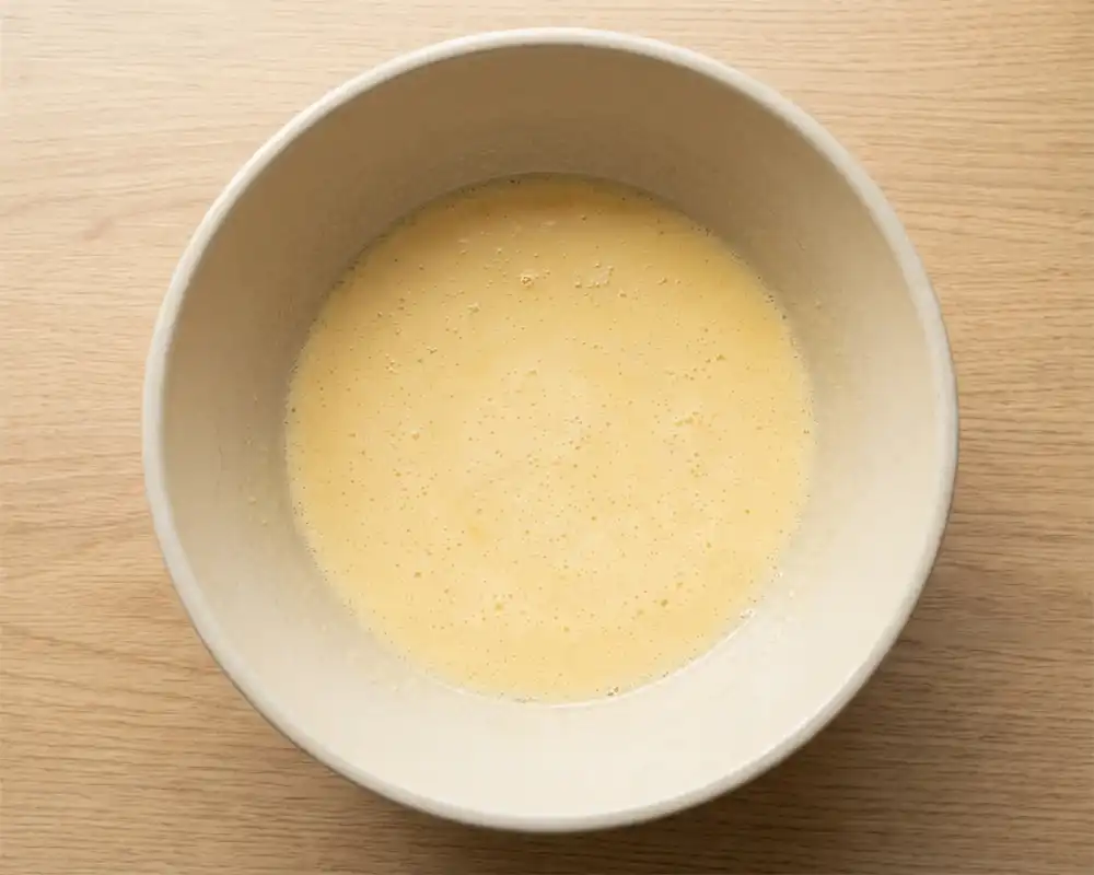 Glatt verquirlte Eierbasis für Spinat-Feta-Muffins in einer hellbeigen Keramikschüssel von oben fotografiert.