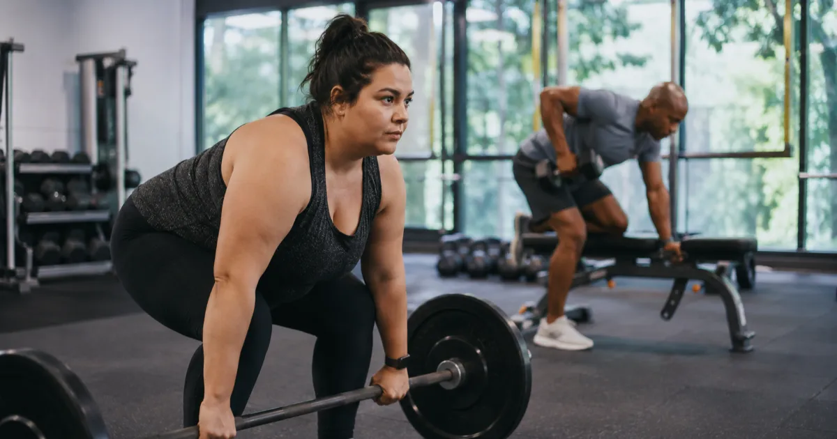 Frau beim Langhanteltraining und Mann beim Kurzhantelrudern im Fitnessstudio