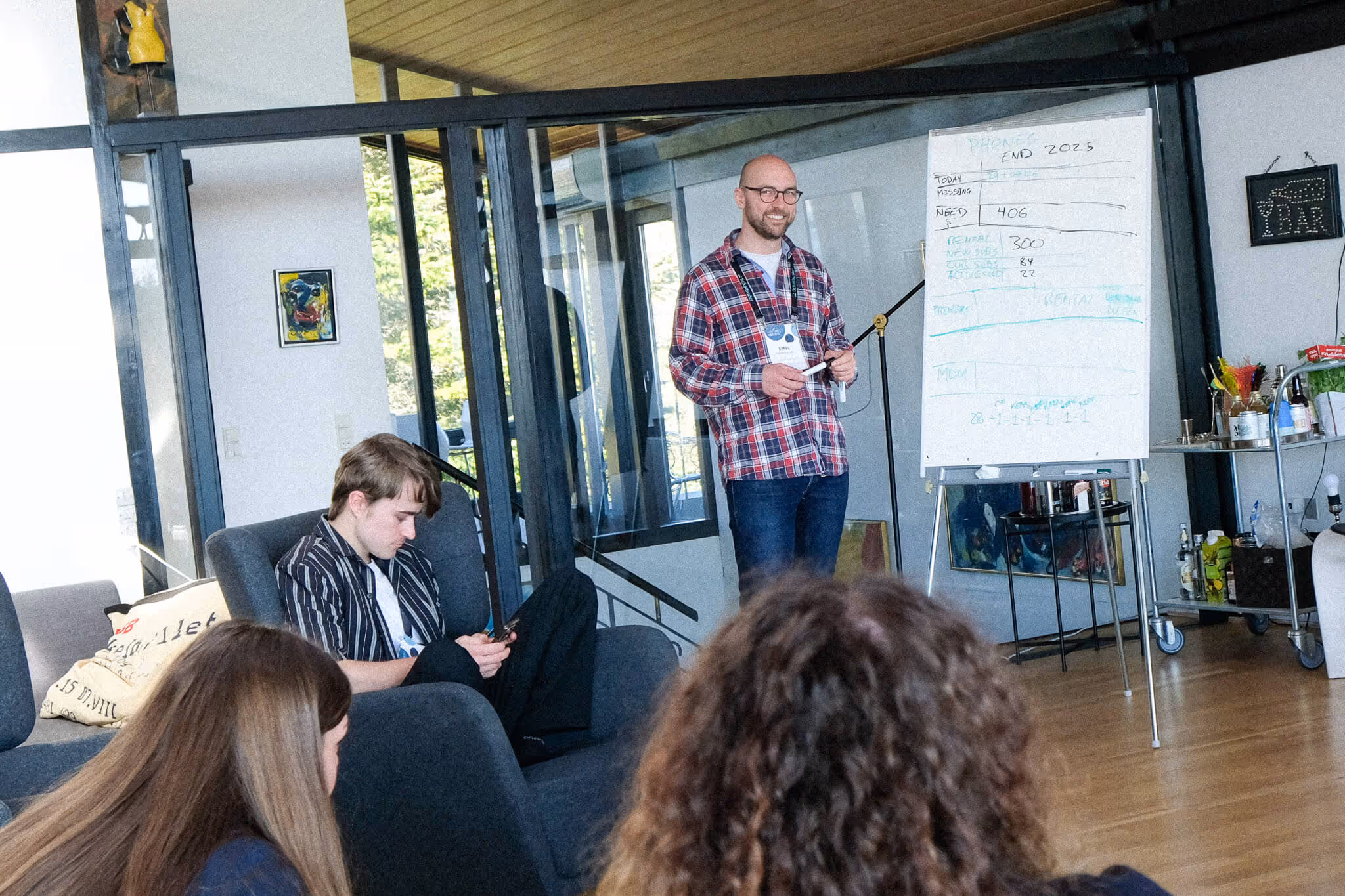 Emil Kjer in plaid shirt presenting information on a whiteboard to seated young adults in a modern room.
