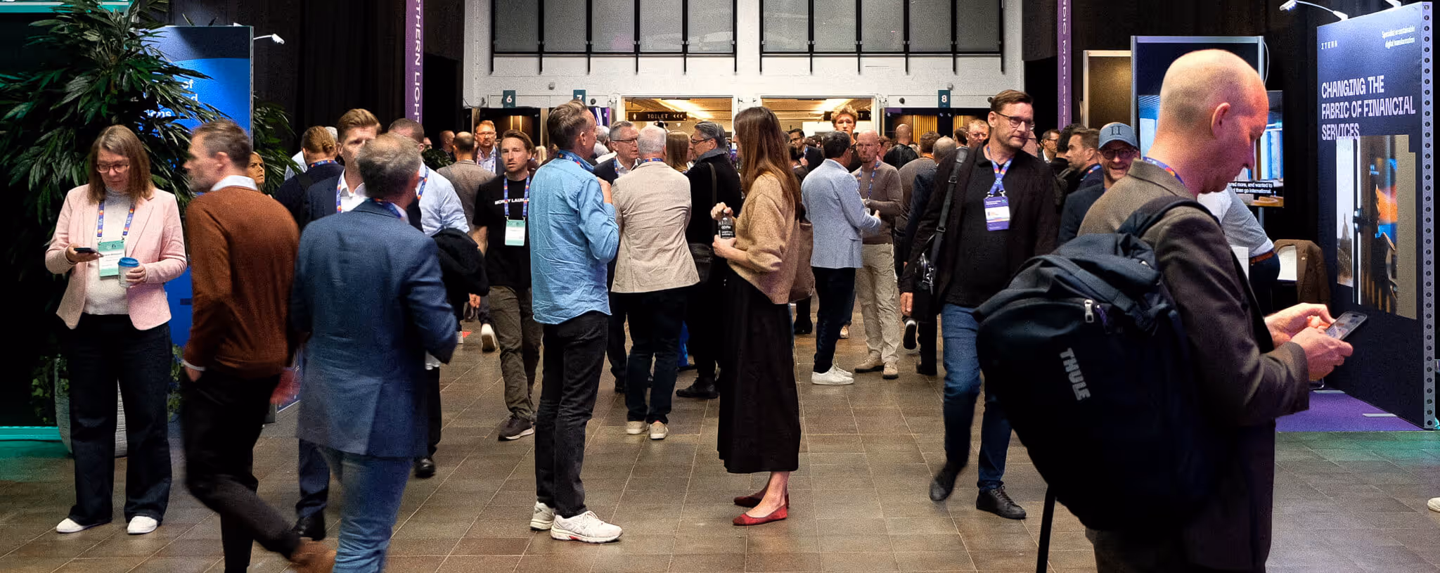 Crowd of people networking and walking in a conference hall with informational booths. On-site name badge printing. hifredo.com