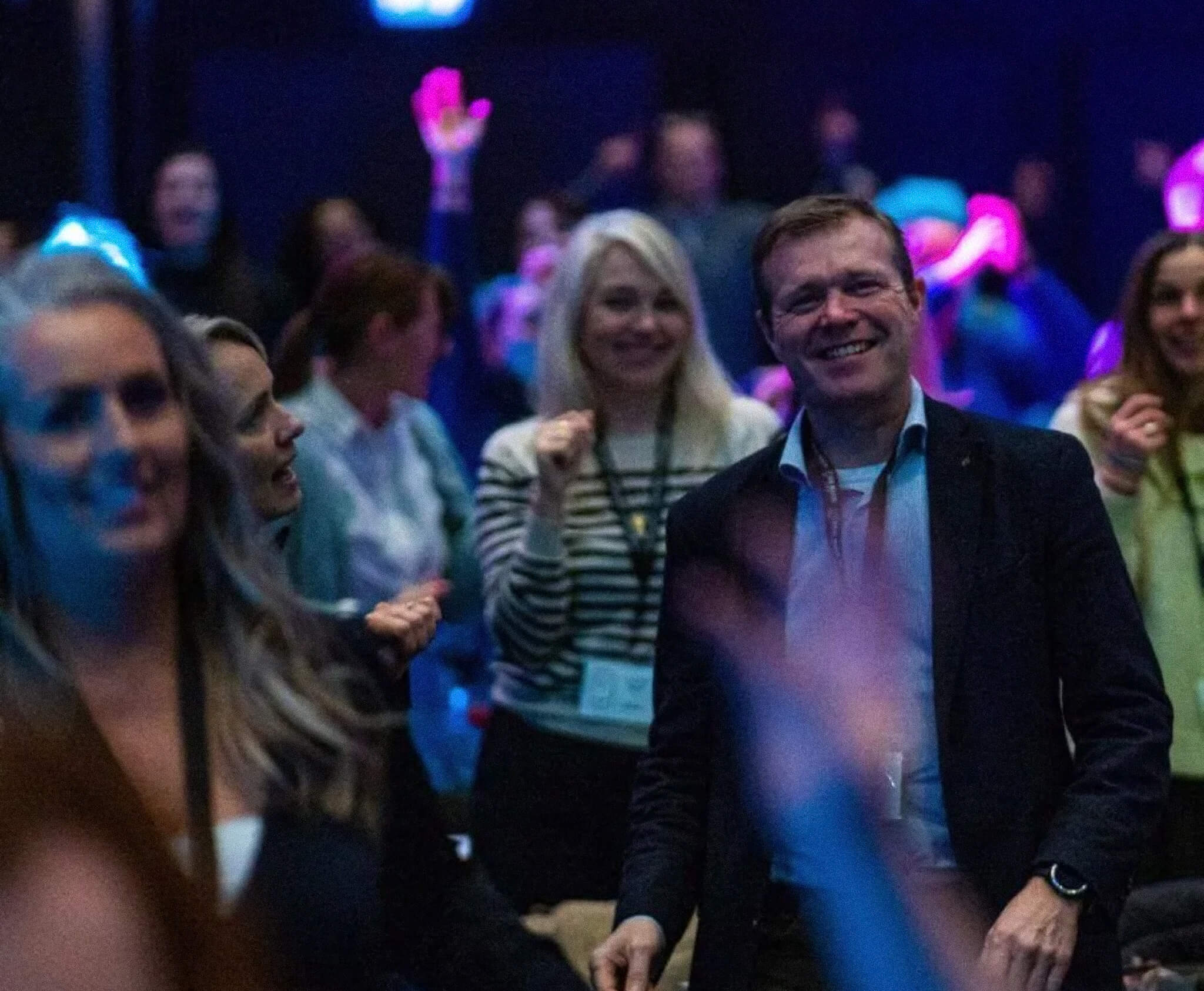 Group of people smiling and celebrating at an indoor event with blue and purple lighting.