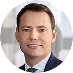 Portrait of a man in a suit and tie with a blurred office background.