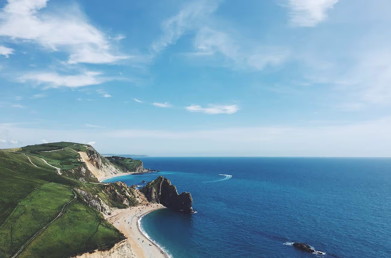 A beach with cliffs and a large rock formation beside the blue ocean under a clear sky.