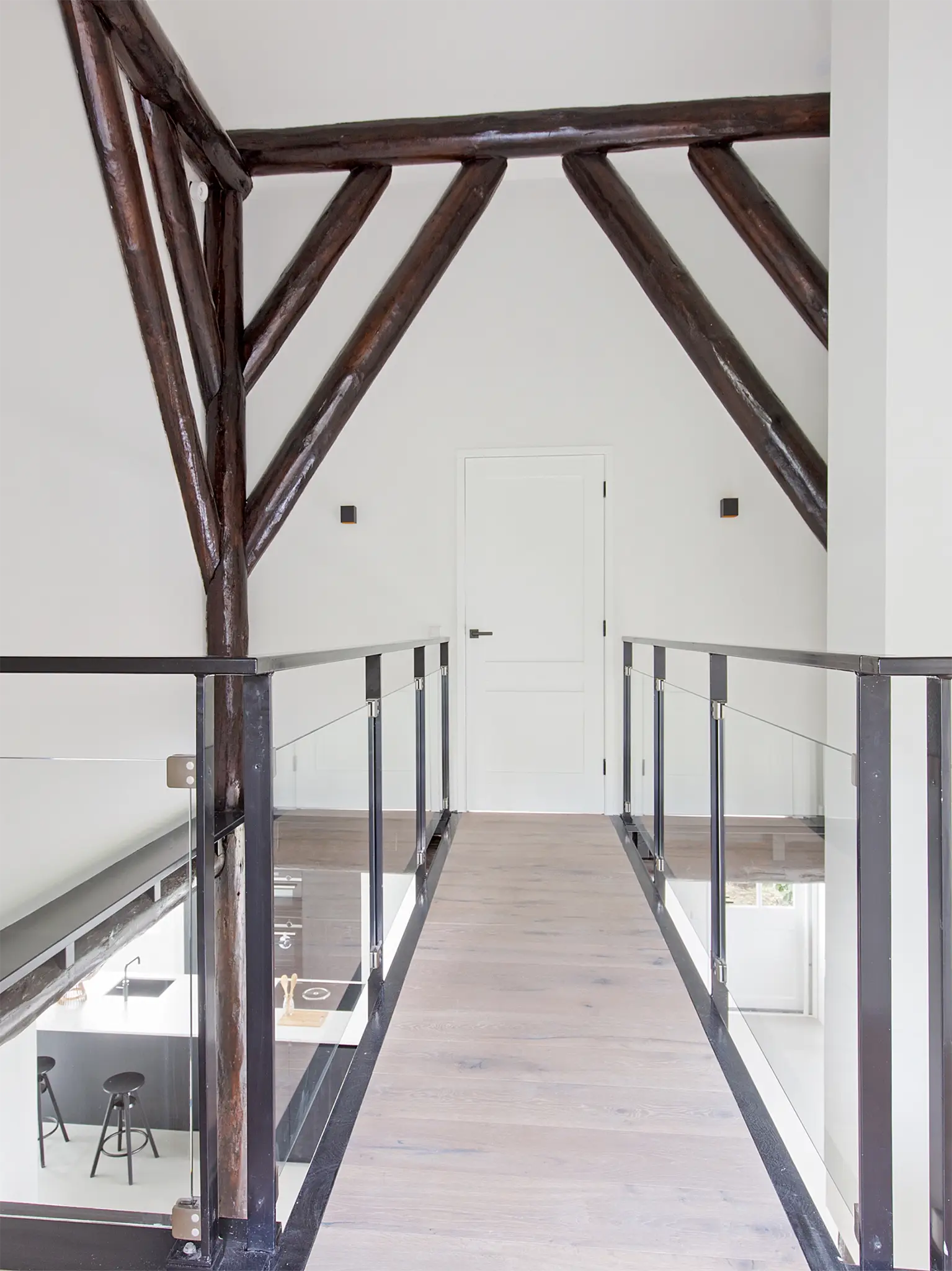 Moderne overloop met railing van metaal en glas, in combinatie met traditionele houten balken in een boerderij.