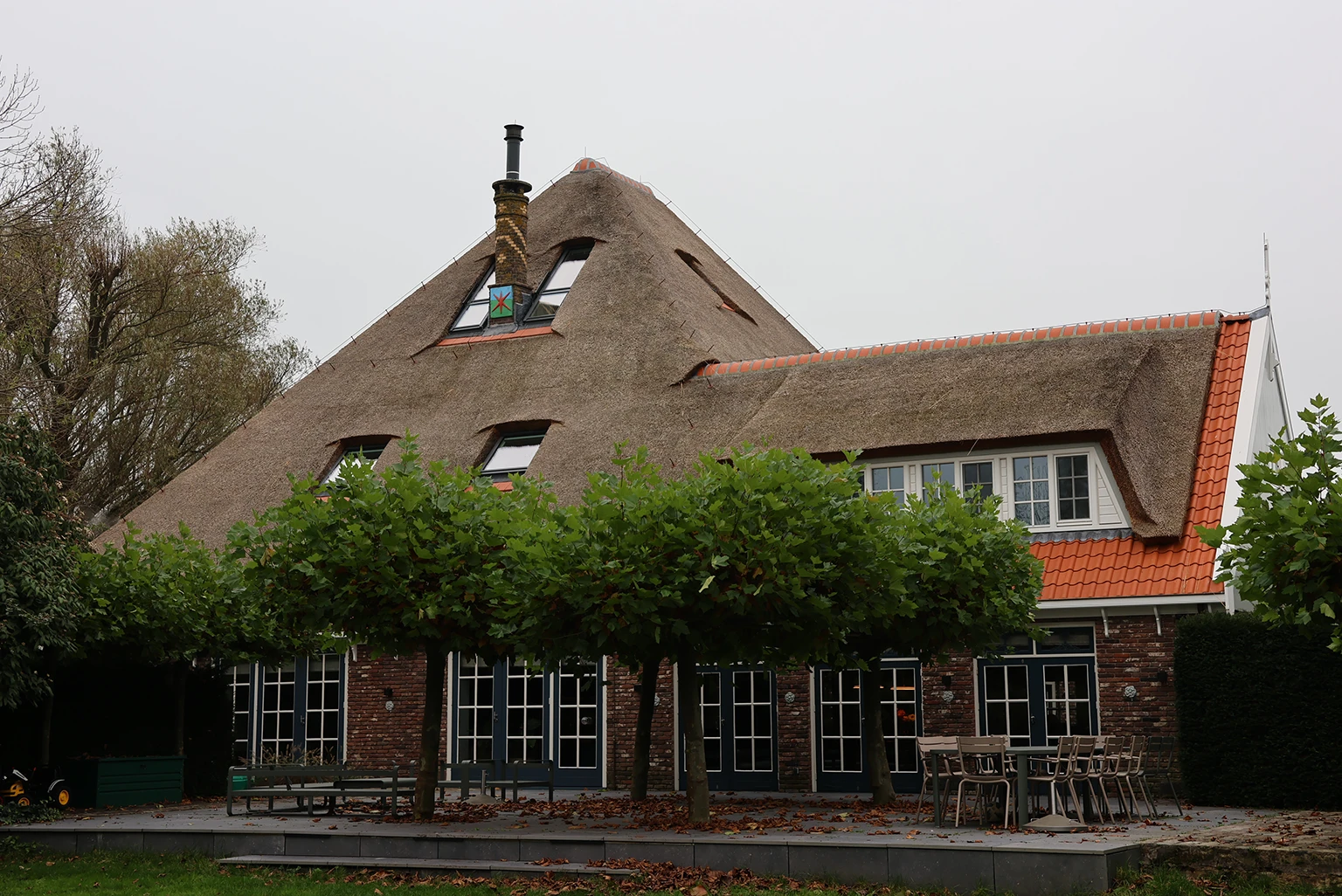 Sfeervolle bovenverdieping van een gerenoveerde boerderij met een donker houten visgraatvloer, rustieke houten balken en moderne zwarte inbouwkasten. Een vintage houten ladekast met een kleurrijk boeket bloemen voegt warmte en karakter toe aan de ruimte.