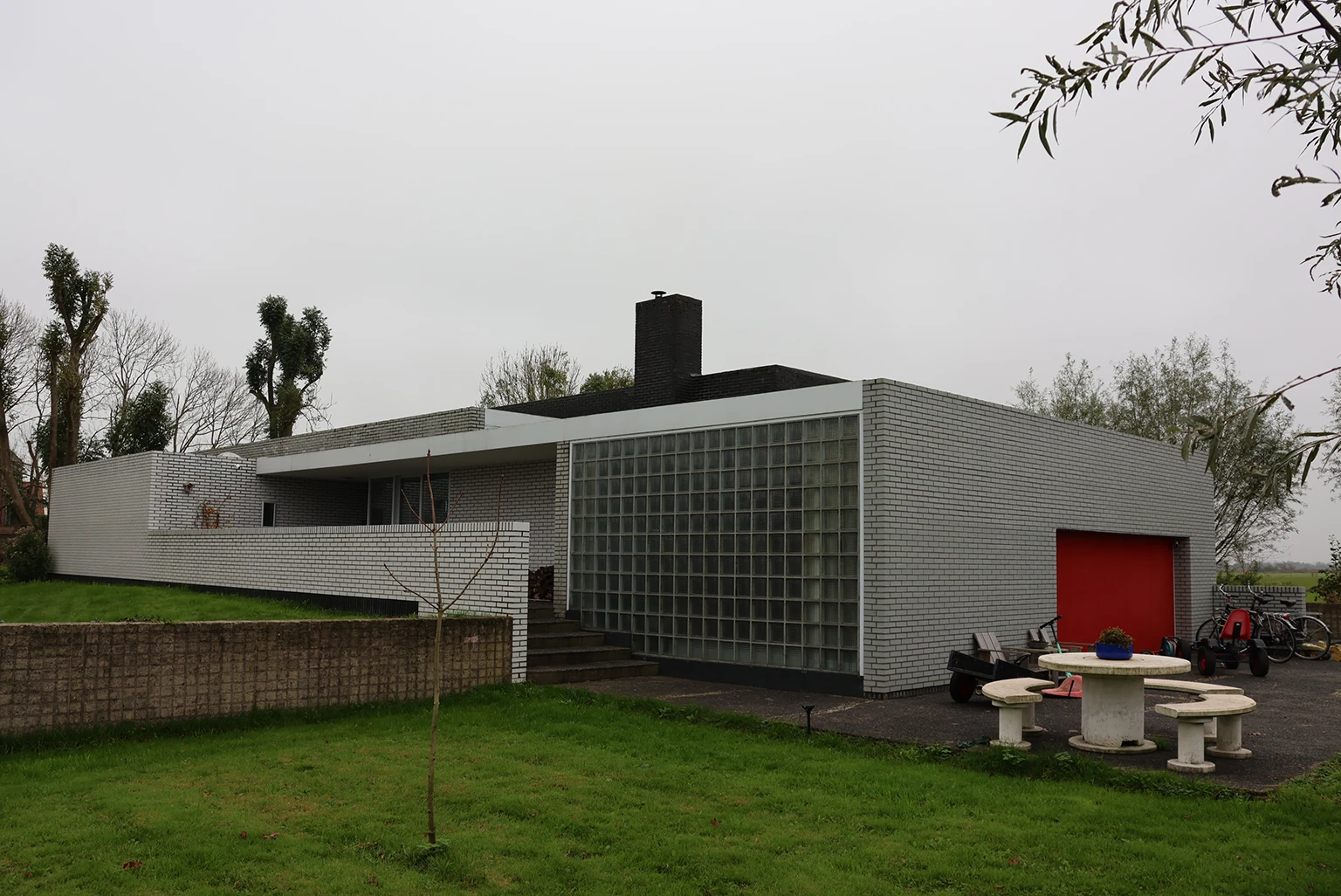 Verbouwing van een moderne woning met een lichte, open ruimte, glazen schuifdeuren en een stijlvolle keuken. Het plafond is voorzien van vierkante lichtpanelen, terwijl de inrichting een combinatie van strakke en warme elementen bevat.