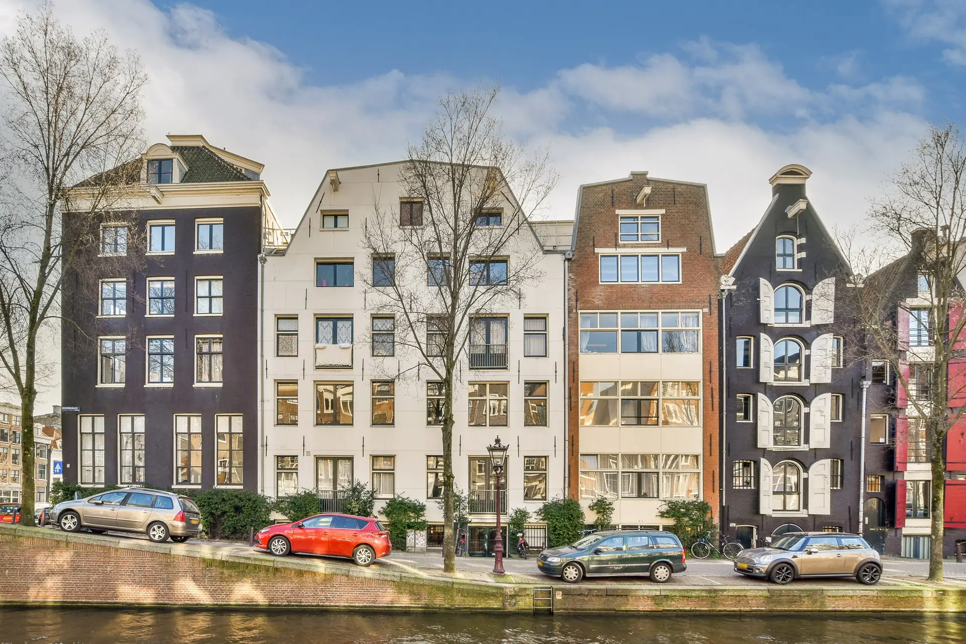 Gerestaureerde historische grachtenpanden aan een Amsterdamse gracht, met een mix van traditionele en moderne architectuur. De gevels tonen karakteristieke details zoals houten luiken, grote ramen en unieke dakvormen.