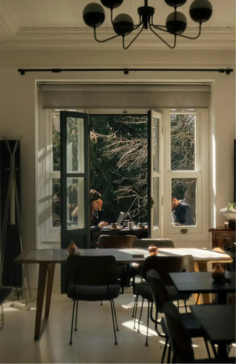 Gezellige woonkamer in Amsterdam. Mensen werken aan een tafel bij openstaande deuren die uitkijken op een groene tuin.