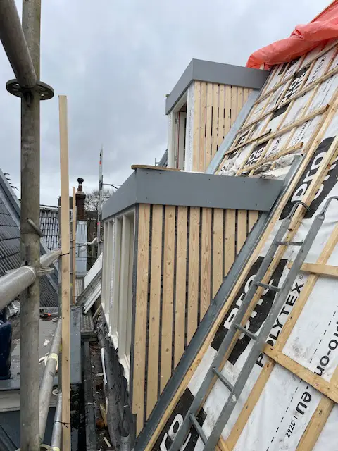 Houten dakopbouw in aanbouw op een Amsterdams pand met steigers en isolatiemateriaal.