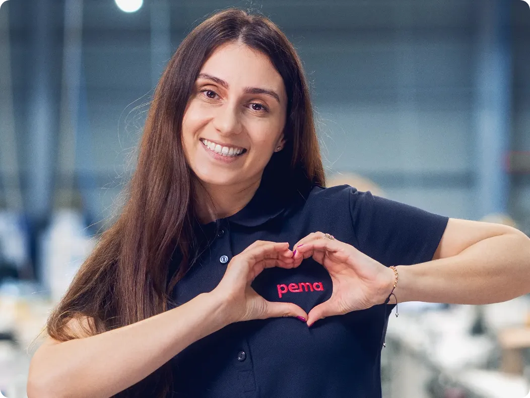 Carmen zeigt mit den Händen ein Herz über dem pema-Logo auf ihrem Shirt.