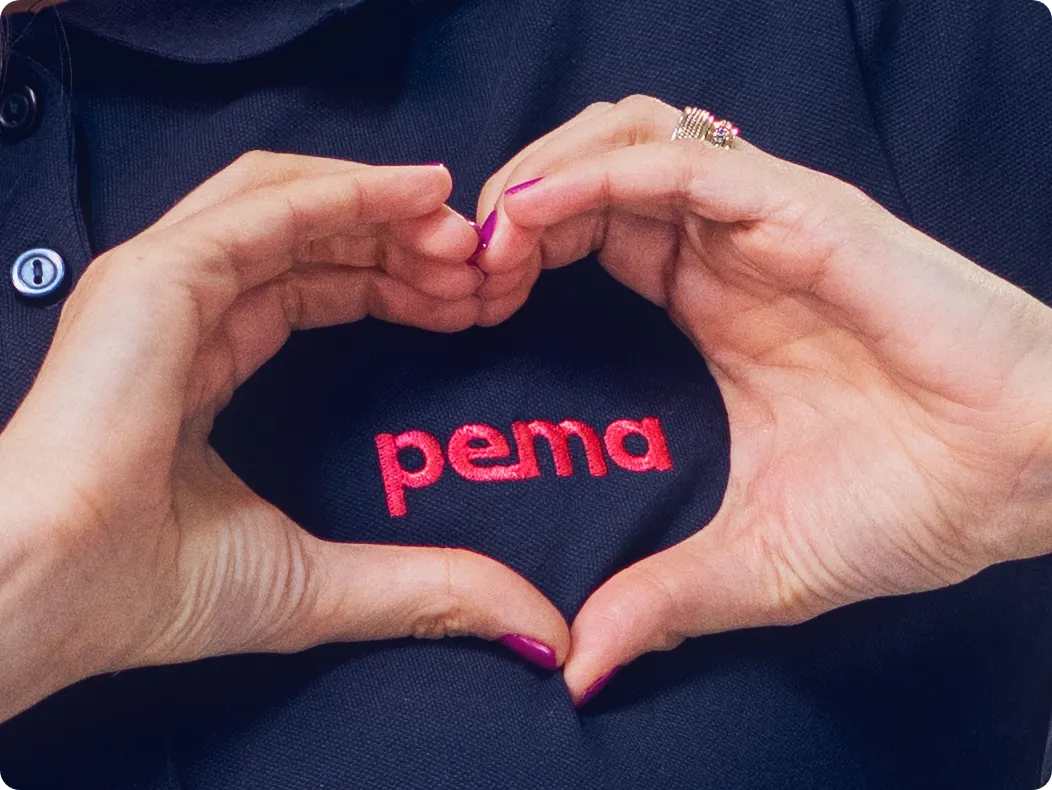 Carmen zeigt mit den Händen ein Herz um das pema-Logo
