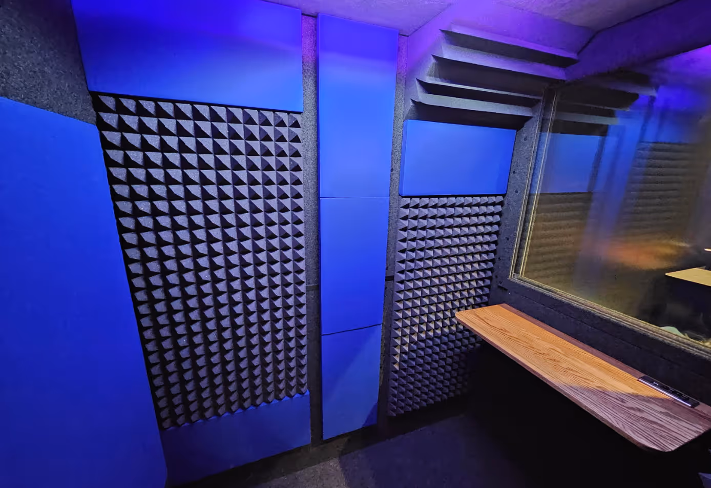 Interior of WhisperRoom 4872 E double-wall sound booth with acoustic foam, blue wall panels, bass traps, office desk, and viewing window.