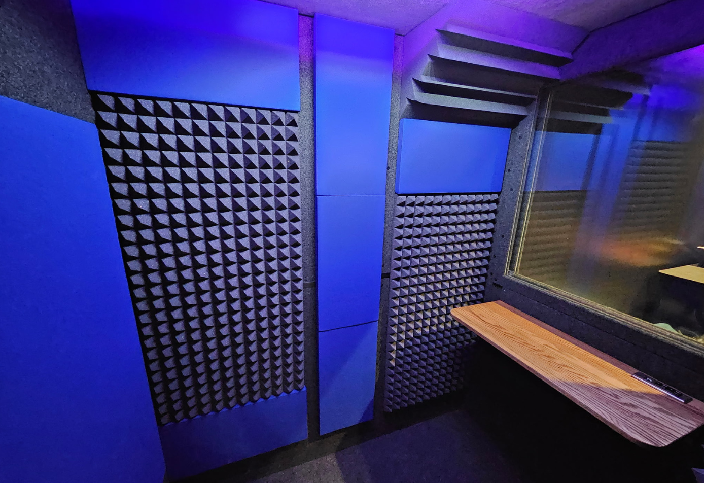 Interior of WhisperRoom 4872 E double-wall sound booth with acoustic foam, blue wall panels, bass traps, office desk, and viewing window.