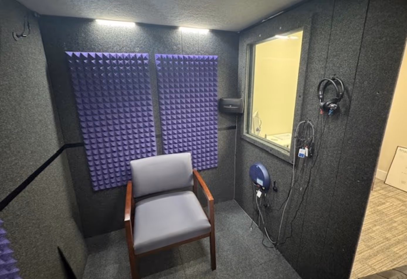Audiology Premium WhisperRoom at Naples Hearing Center with purple acoustic foam, patient chair, testing equipment, and observation window.