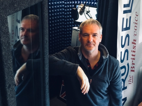 Voice actor inside a WhisperRoom voice over booth with professional acoustic treatment and microphone setup.