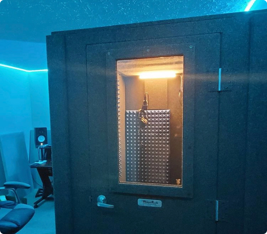 WhisperRoom sound isolation booth with sealed door and microphone setup visible through the window.