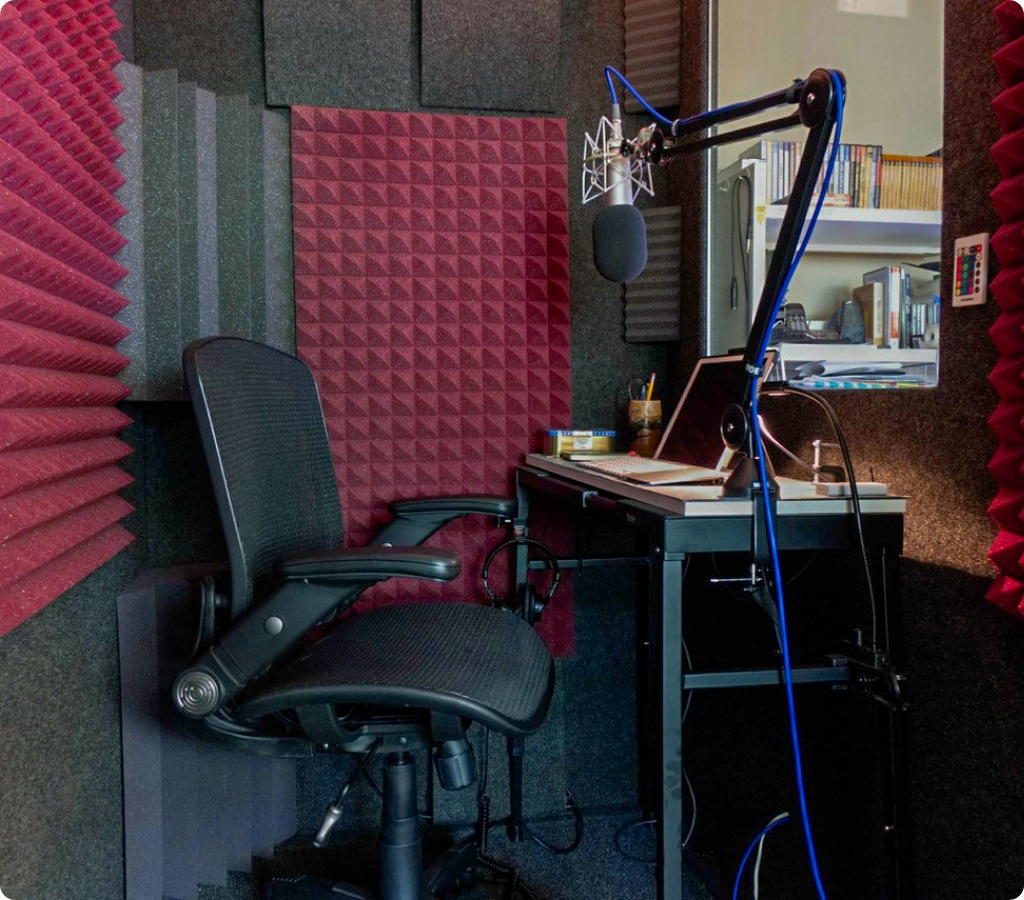 A fully equipped WhisperRoom booth interior with a boom arm microphone, laptop workstation, and acoustic treatment panels.