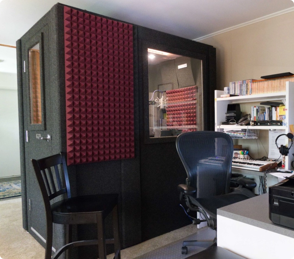 Exterior view of a WhisperRoom booth showing its footprint, window, and acoustic treatment panels in a home studio.