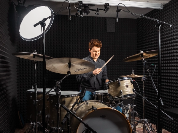 Drummer recording inside a WhisperRoom booth featuring acoustic foam, overhead mics, and controlled studio lighting for professional drum isolation.