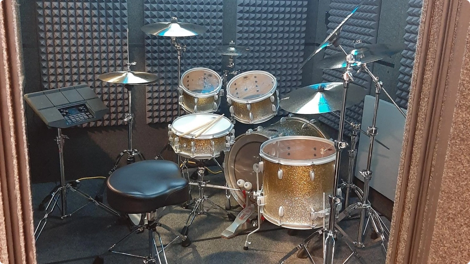 Drum kit inside a WhisperRoom sound isolation booth with acoustic foam panels and overhead lighting.