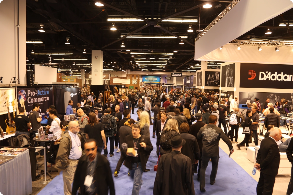 Crowded trade show floor with exhibitors and attendees navigating a noisy, high-traffic convention hall