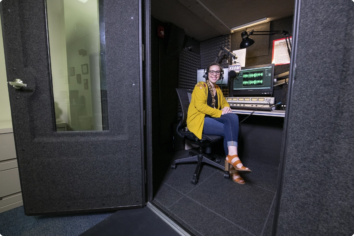 a female creator next to recording gear inside a WhisperRoom Broadcast Booth