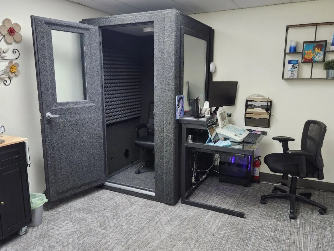 WhisperRoom audiometric testing booth installed in a hearing clinic with audiology equipment and an adjacent testing workstation.