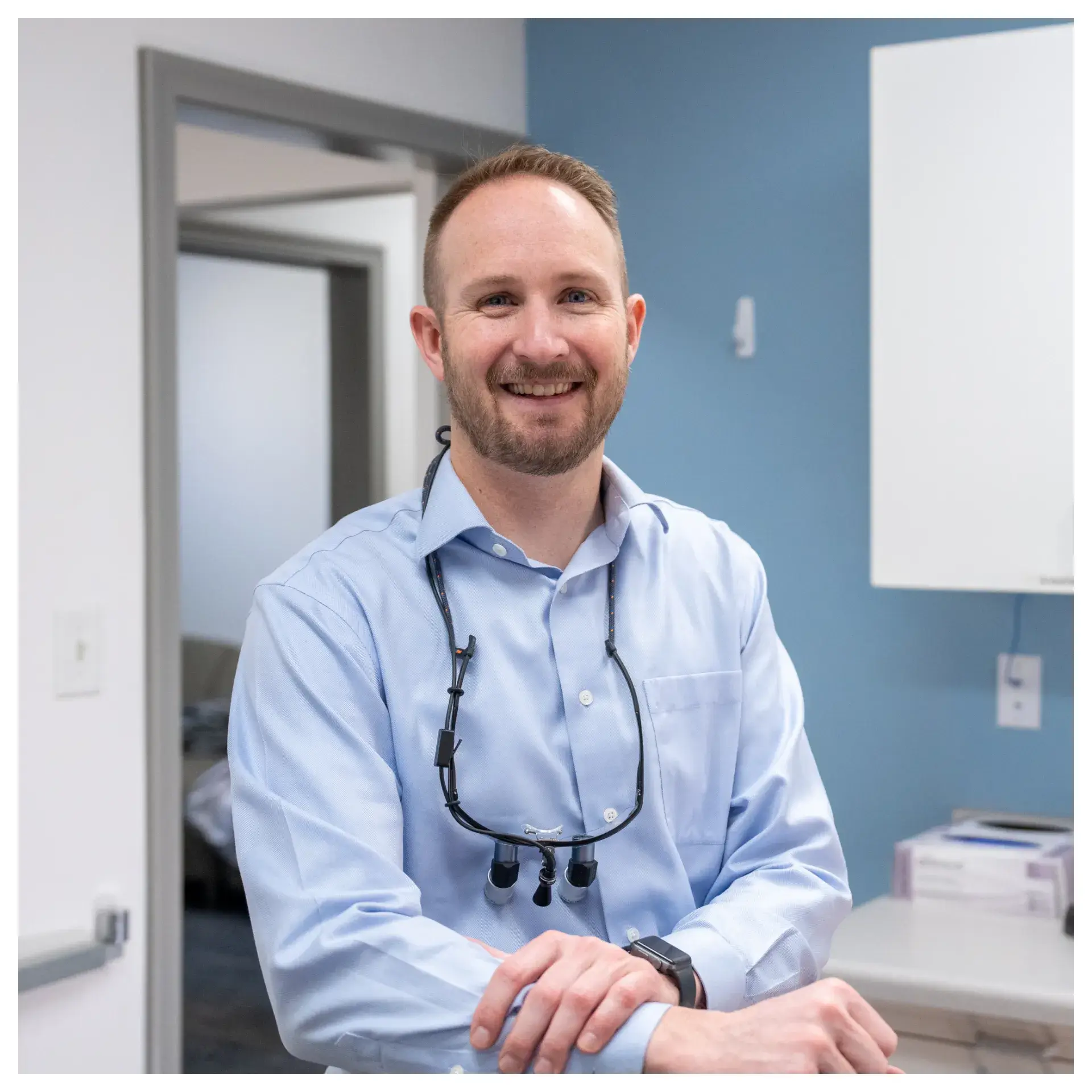 A man in a light blue shirt smiles in a dental office setting.
