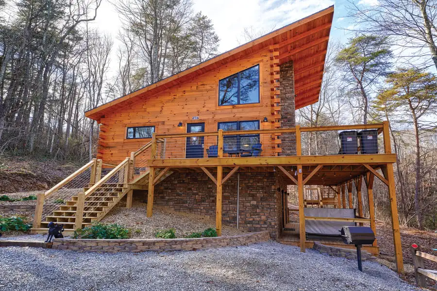 Exterior view of the Sleepy Hollow log home by Hochstetler Log Homes, featuring natural wood siding, large windows, and wraparound deck set in a wooded landscape.
