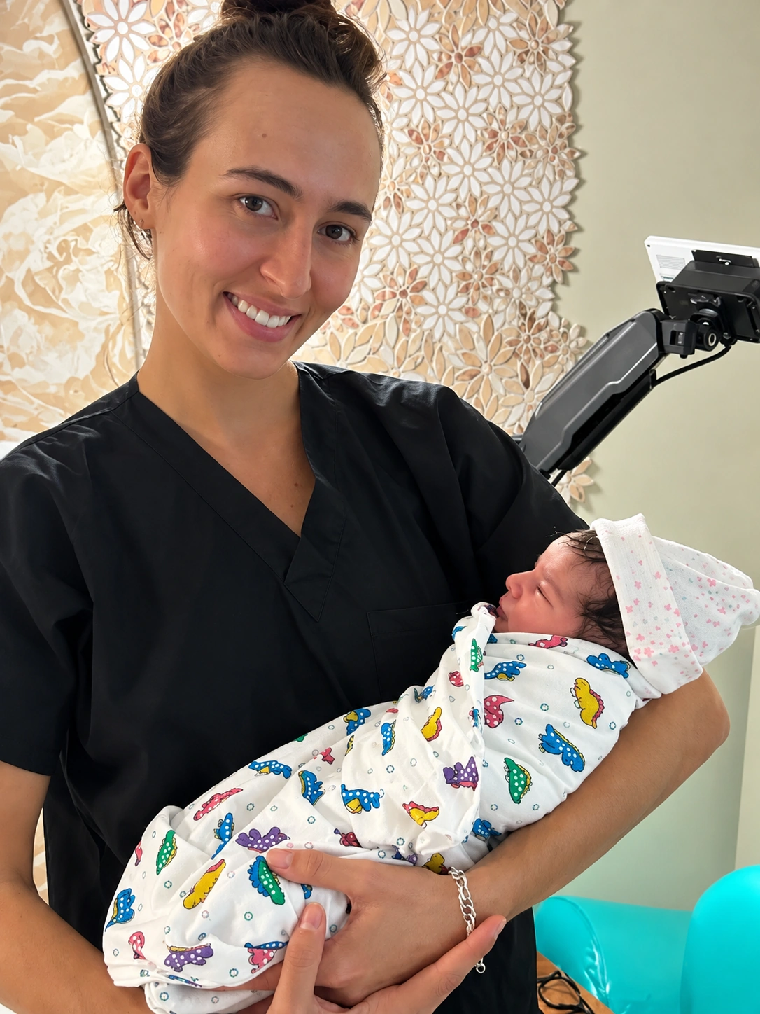 Smiling woman in dark scrubs holding a swaddled newborn baby