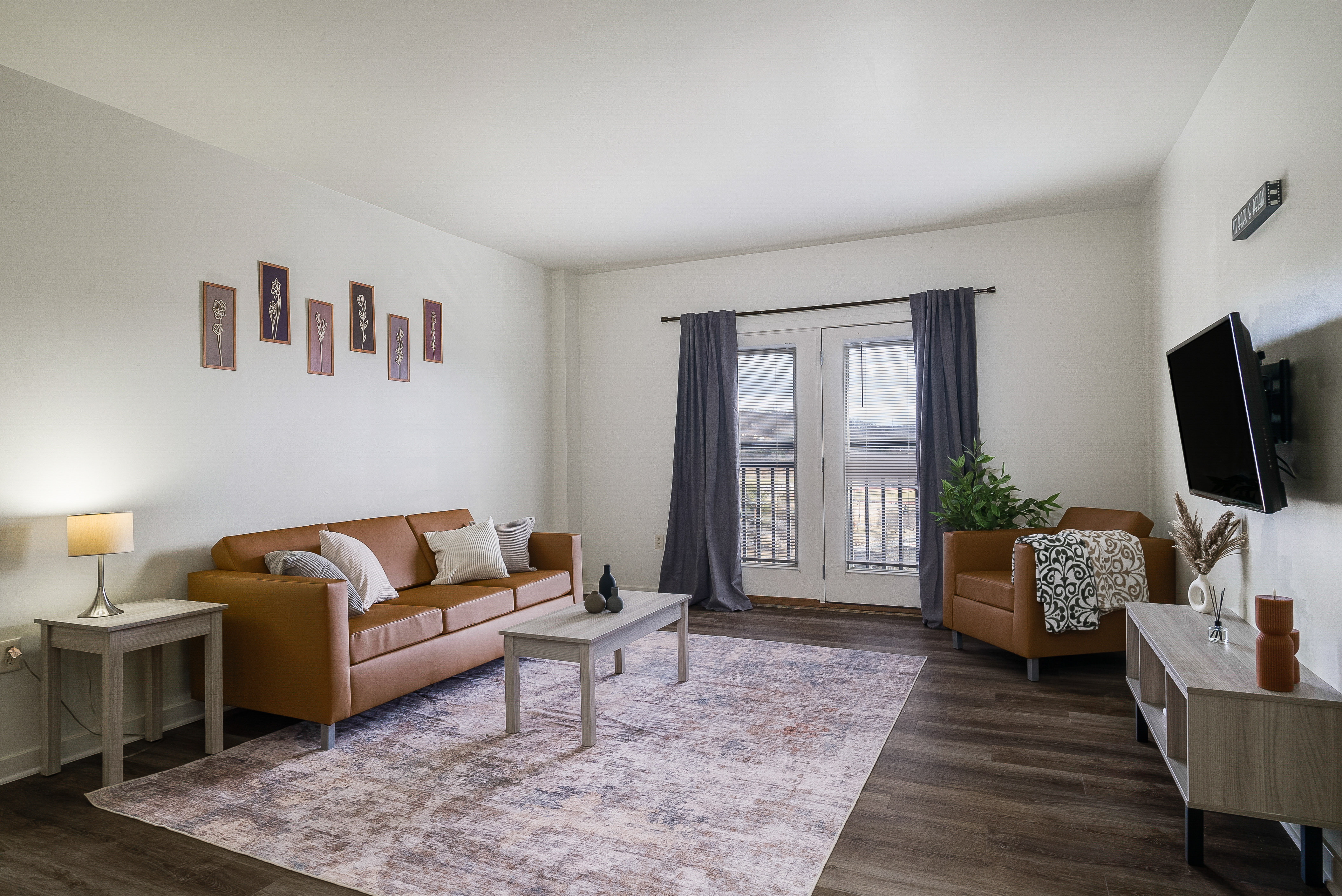 Living room with sofa, rug, coffee table, and tv and view of balcony doors with curtains