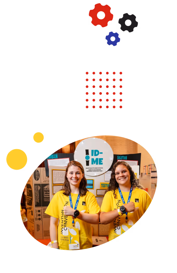 Two smiling teen girls, wearing Invention Convention shirts, bumping elbows while standing in front of their invention poster