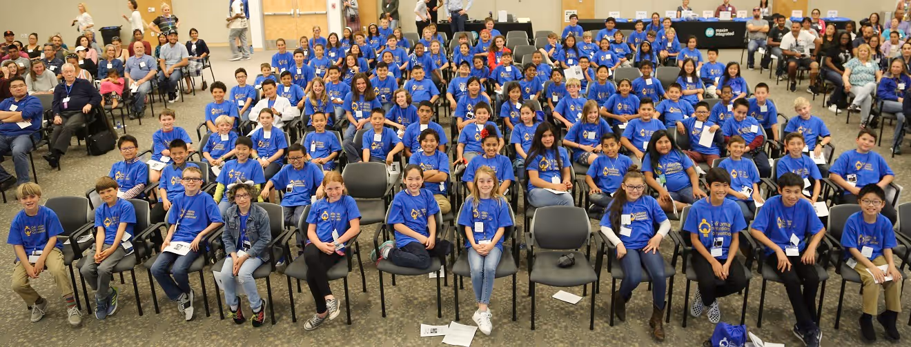 A large group of young kids with yellow shirts and red lanyards in a large room