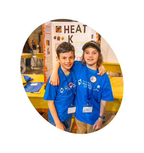 Two smiling young boys in a CAIC shirt, standing in front of their invention poster board