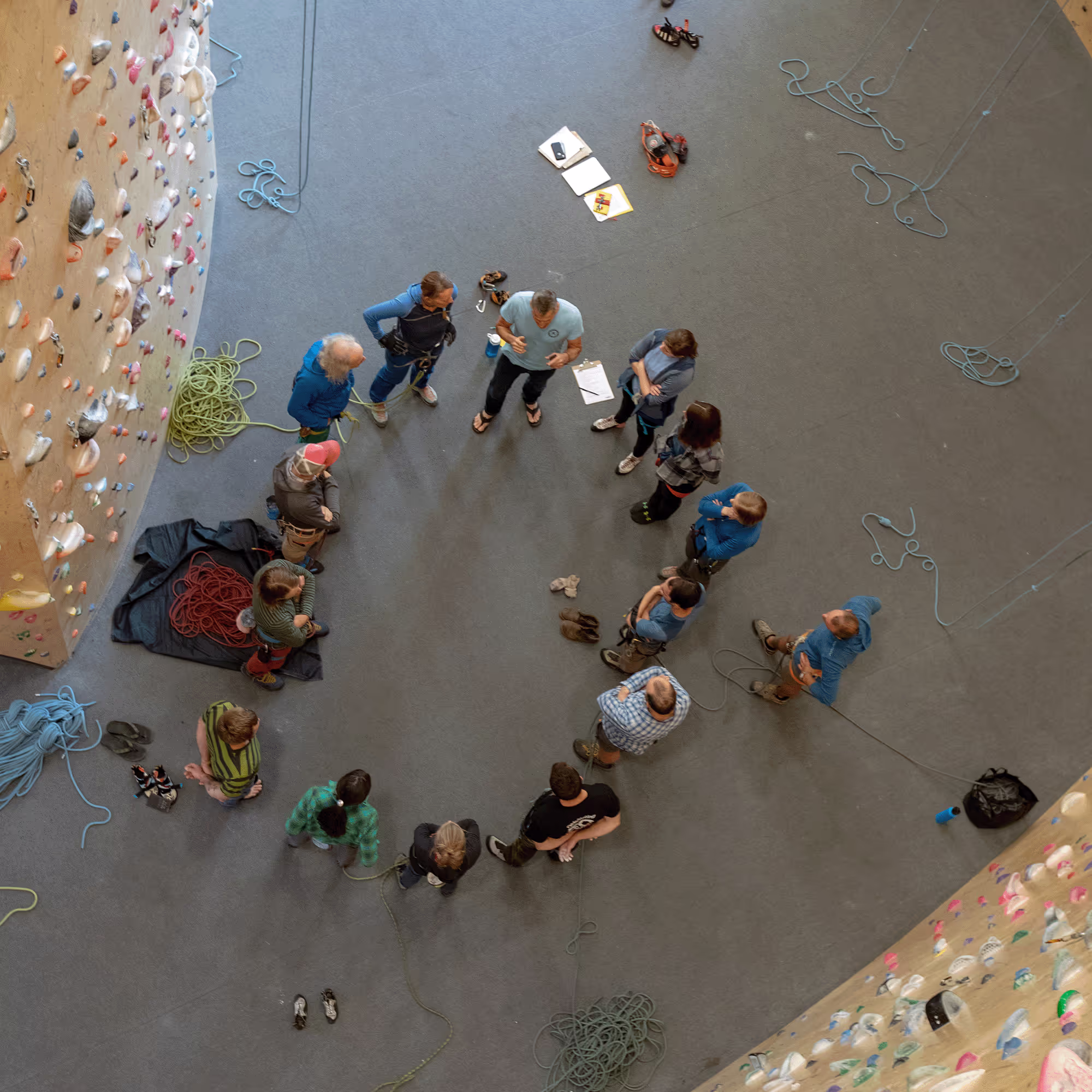 A group of people standing in a circle on an indoor climbing gym floor.