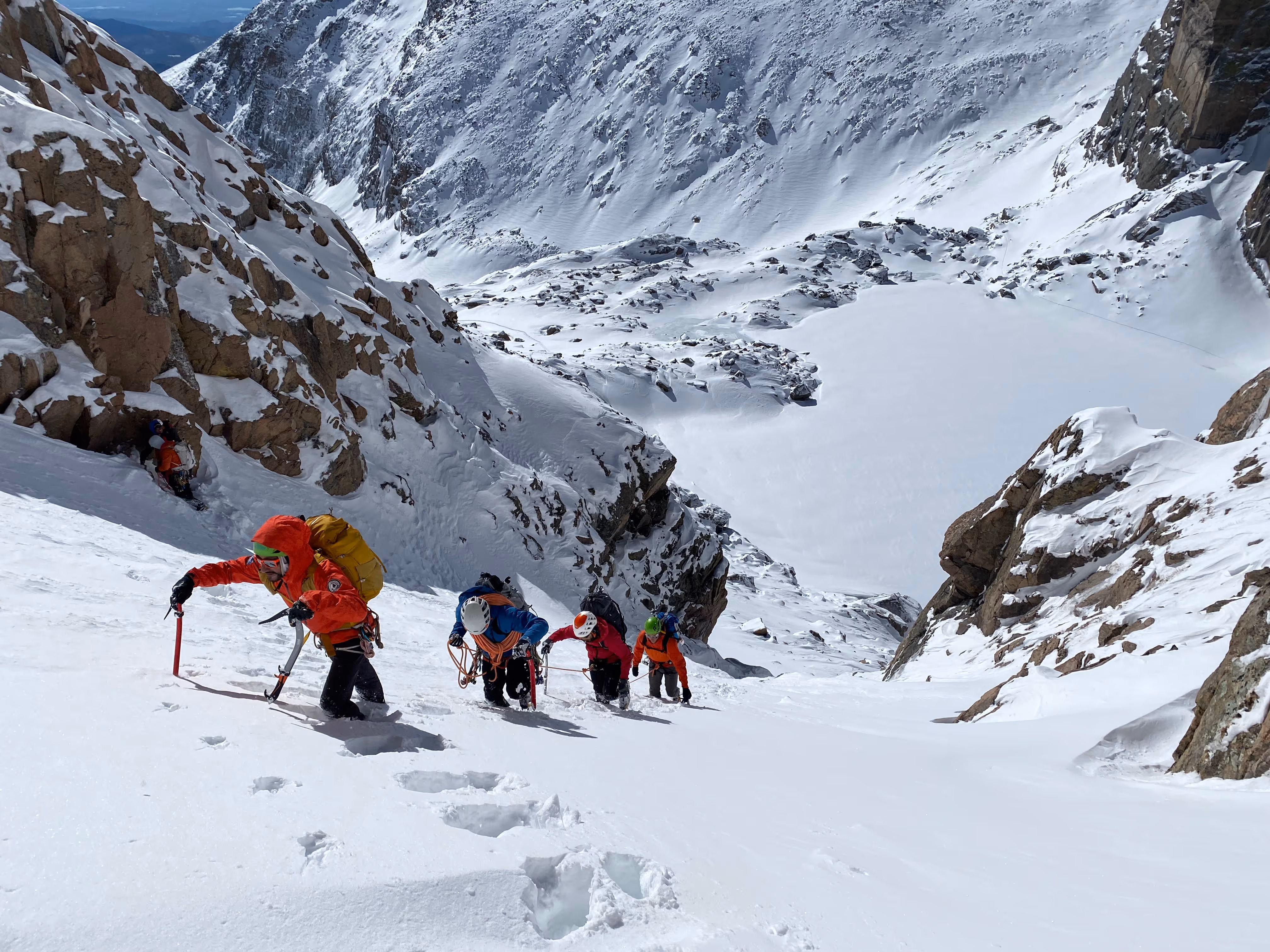 A group of climbers in colorful gear ascends a snowy mountain slope.