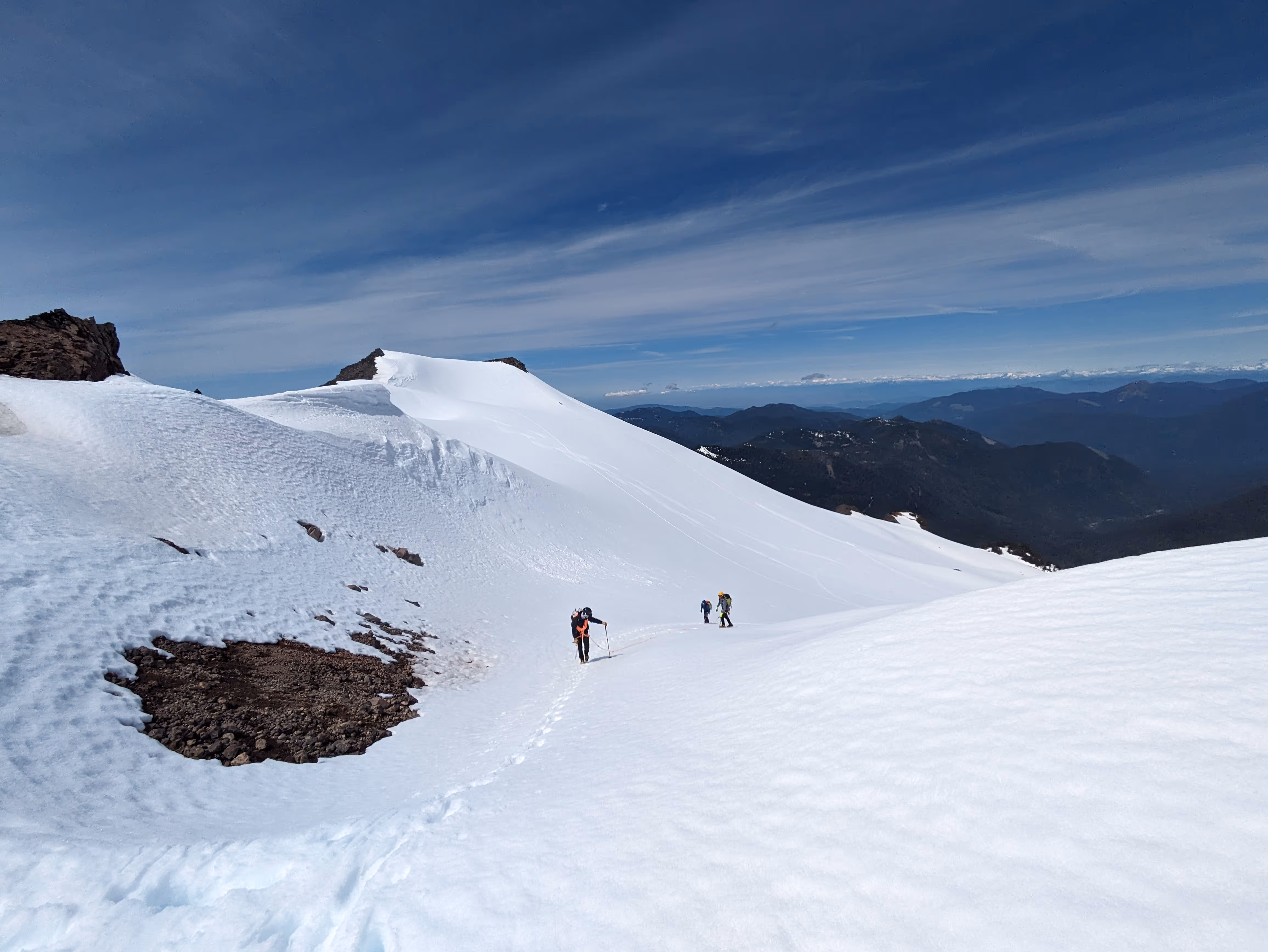 Three people hiking up a snowy mountain under a clear blue sky.