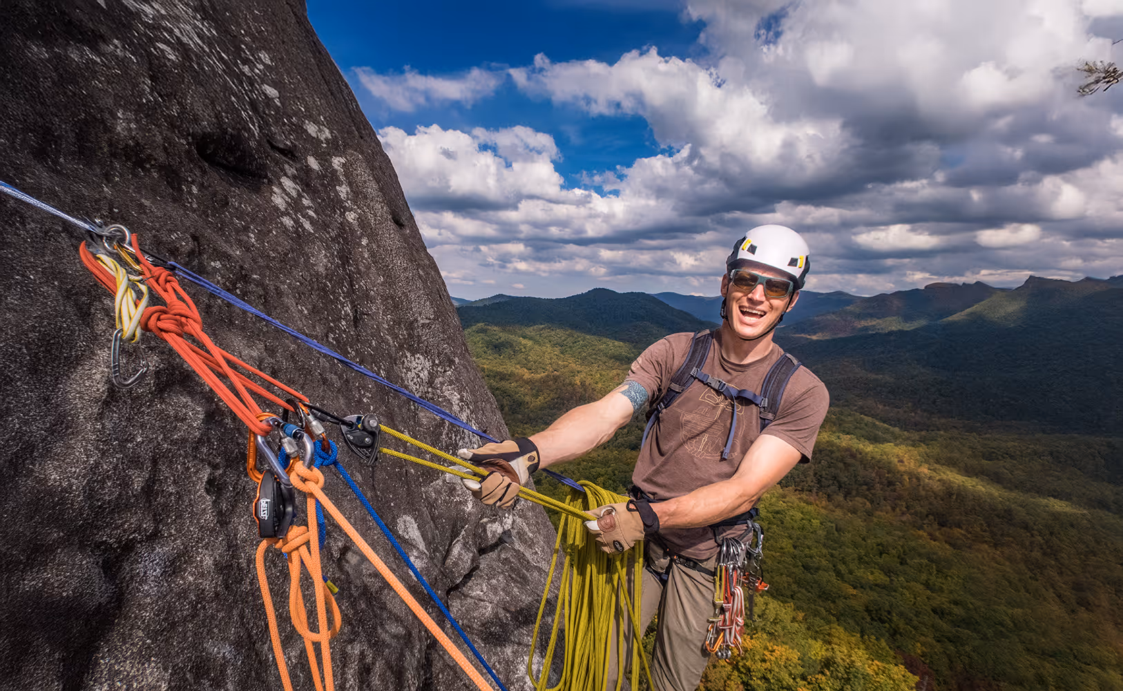 A climber wearing a helmet is securely attached to ropes while ascending a steep rock face.
