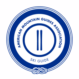 Blue and white circular logo for the American Mountain Guides Association, featuring two skis in the center.