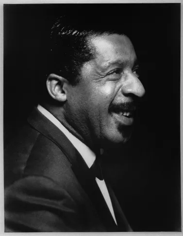 Black and white portrait of a smiling Erroll Garner in profile wearing a suit and bow tie.