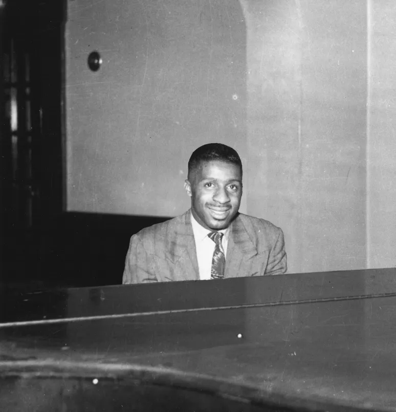 Black and white photo of Erroll Garner in a suit sitting behind a piano.
