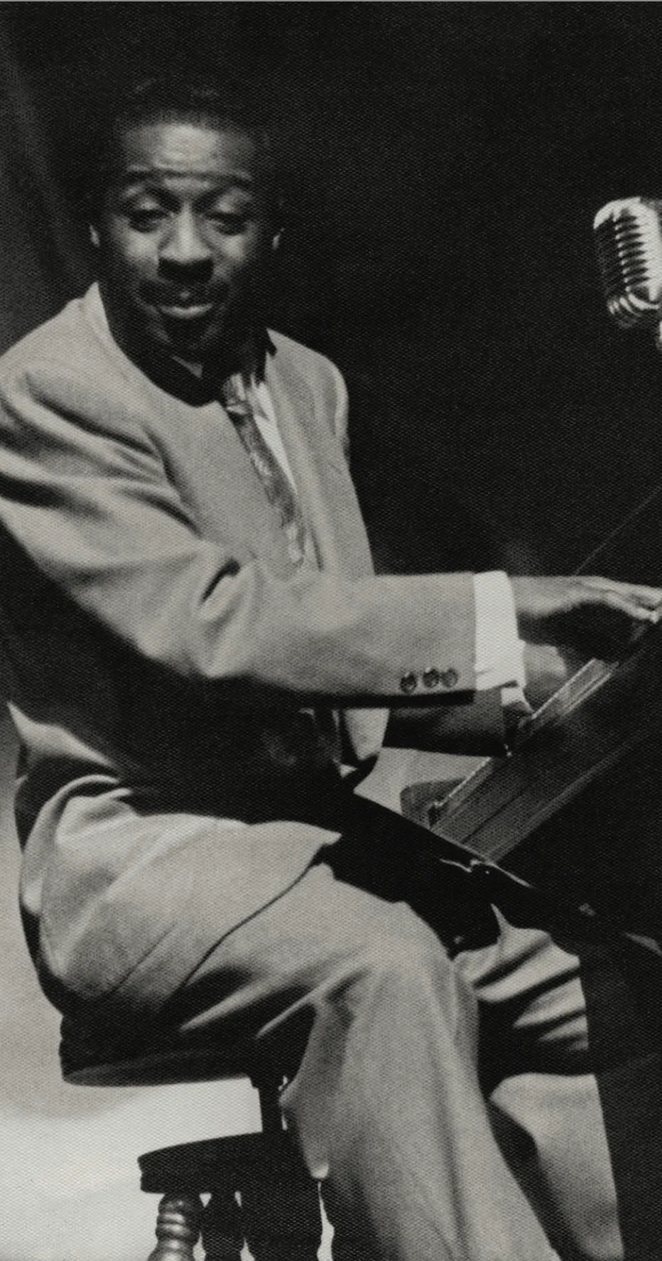 Black and white photo of Erroll Garner in a suit playing a piano with a vintage microphone nearby.