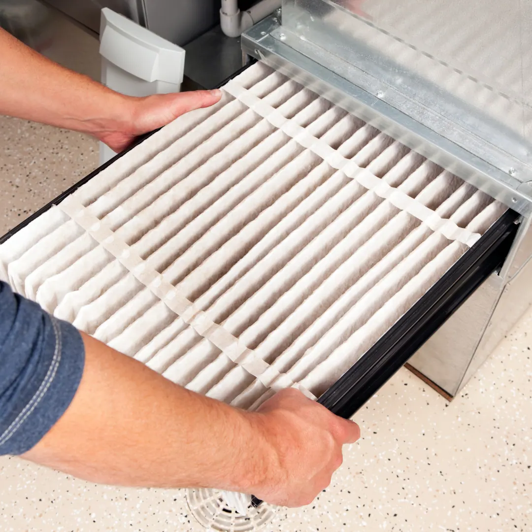 Hands lifting a pleated air filter out of a furnace slot