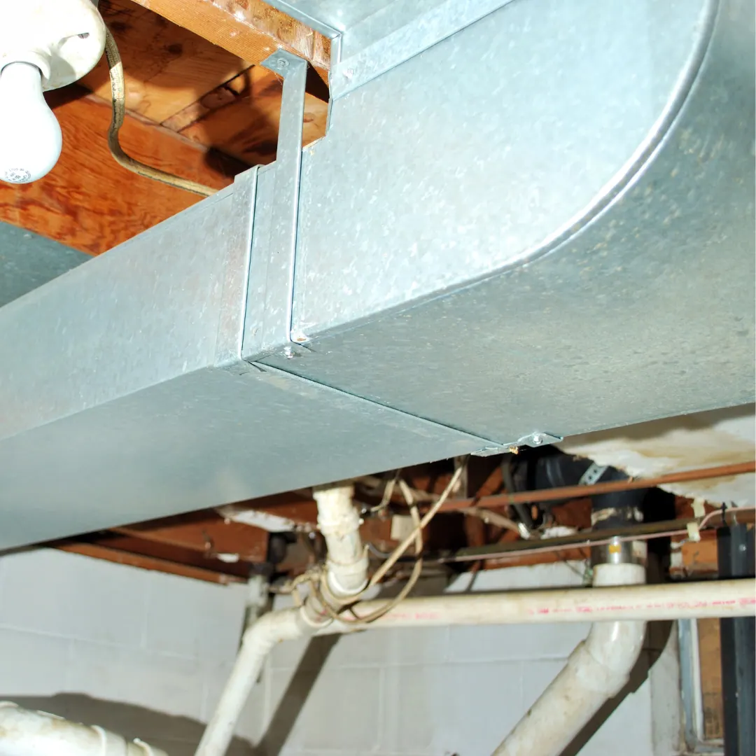 Metal ductwork running across a basement ceiling above pipes