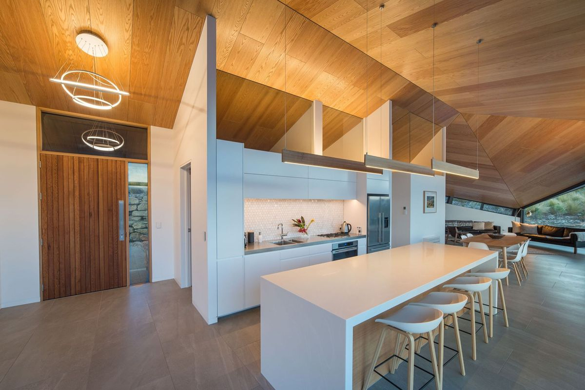 Open-plan kitchen with a pitched timber ceiling, white island and bar stools.