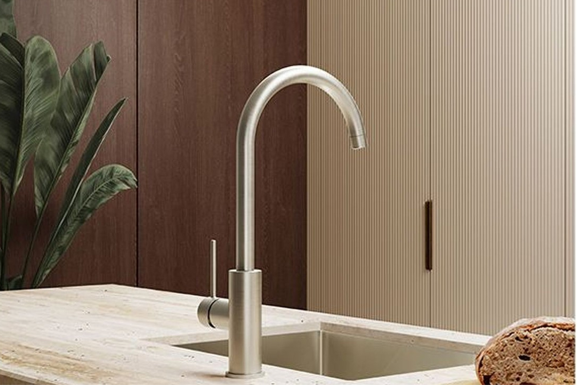 Brushed-metal gooseneck kitchen tap above a stainless-steel sink in a stone benchtop.