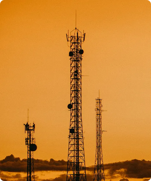 Three communication towers silhouetted against an orange sky at sunset.