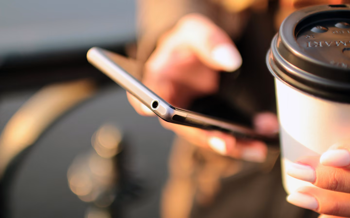 Close-up of hands holding a smartphone and a takeout coffee cup with a black lid.